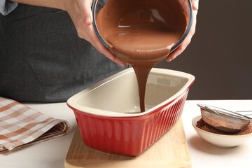 Woman pouring liquid chocolate dough into baking dish at light wooden table, closeup