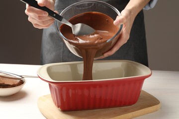 Woman pouring liquid chocolate dough into baking dish at light wooden table, closeup
