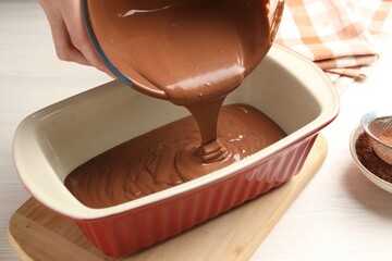 Woman pouring liquid chocolate dough into baking dish at light wooden table, closeup