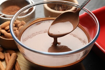 Taking liquid chocolate dough with spoon from bowl at table, closeup