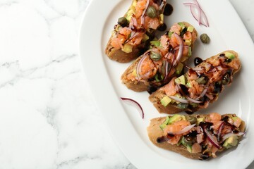 Delicious bruschettas with salmon, avocado, capers, onion and sauce on white marble table, top view. Space for text