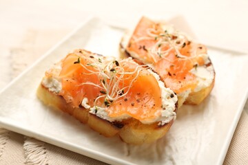 Tasty bruschettas with salmon, cream cheese and microgreens on light table, closeup