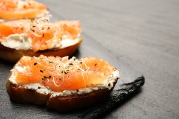 Tasty bruschettas with salmon, cream cheese and microgreens on black table, closeup. Space for text