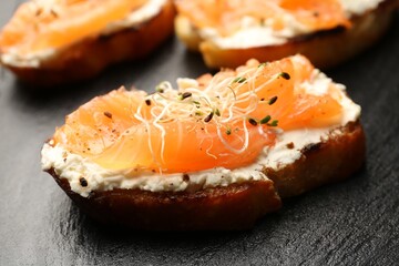 Tasty bruschettas with salmon, cream cheese and microgreens on black slate board, closeup