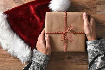Closeup of a soldier holding a Christmas present with a Merry Christmas tag on a wood table and a...