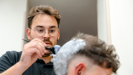 Barber carefully bleaching client's hair in modern shop