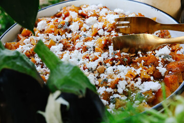 Close-up of Rustic Roasted Butternut Squash and Vegetable Salad Topped with Crumbled Feta Cheese and Chopped Hazelnuts, Served with Golden Tongs
