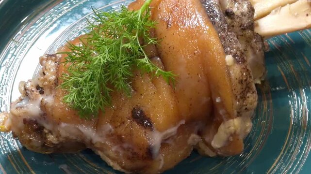 Golden brown pork knuckle with crispy skin is served with a sprig of dill