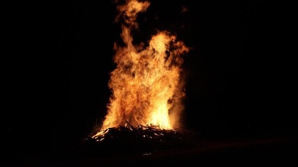 bonfire flames rising into dark night sky (bon fire flame orange yellow red glow glowing ember) sticks wood stick brush wooden fuel summer ceremony celebration enormous huge rise heat campfire camping