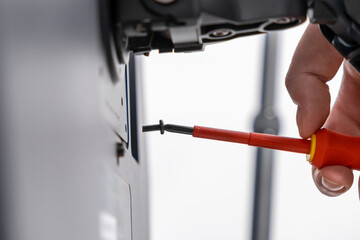 Hand holding an insulated red screwdriver to meticulously fasten a black screw into a technical...