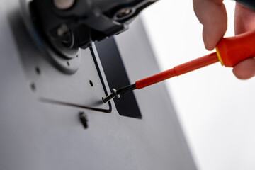 Skilled hand meticulously uses an insulated red screwdriver, fastening a small black screw into a modern device component for assembly and professional technical repair