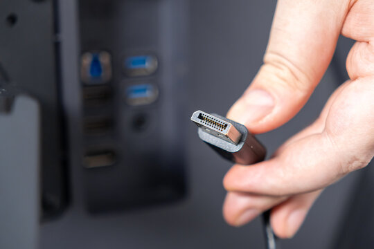 Person holds DisplayPort cable connector, ready to plug into modern computer ports, highlighting digital connectivity and high-resolution display setup