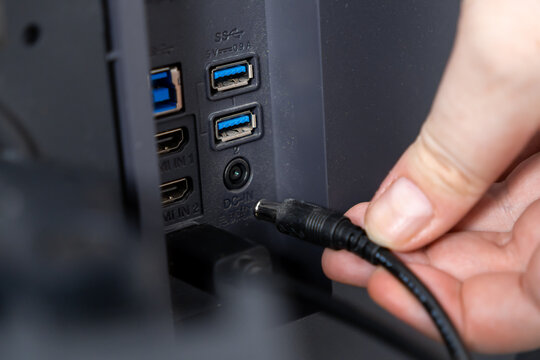 User's hand plugging a black DC-IN power cable into the back panel of a modern electronic device, illustrating essential connectivity and setup