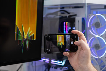 Person's hand using a smartphone to photograph a severely cracked computer monitor screen displaying distorted lines, documenting device malfunction for technical repair