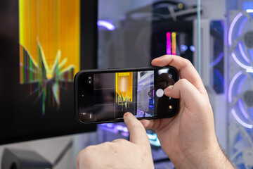 Person's hands film a broken computer monitor with a smartphone, documenting the glitched screen for technical repair and content creation