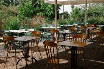 Inviting Rustic Outdoor Dining Area or Restaurant Patio with Wooden Tables, Chairs, and Greenery, Covered by a Large White Umbrella for Shade