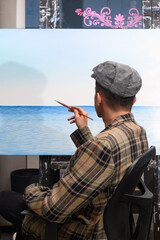 Obraz premium Male artist painting a seascape canvas, viewed from the back