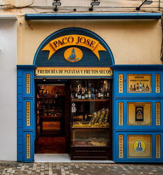 The vibrant, blue and yellow storefront of Paco Jose in Malaga, Spain. The shop sells Fried Potatoes, Dried Fruits, Nuts, and local liquor.