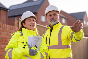 Male construction works project manager and young female site engineer collaborating on-site, discussing project details and future plans at building site