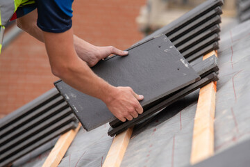 Skilled worker busy applying roofing material on sloped roof focused on securing elements for sturdy structure in bright daylight © Iryna