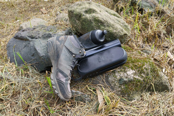 Hiking boot, water bottle, and portable speaker on rocks