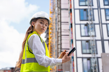 Young woman builder construction manager uses rugged tablet to record data on construction site