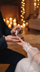 Romantic proposal moment with a man in a suit presenting a velvet ring box to a woman in lace. Surrounded by warm candlelight and string lights, the scene captures love, commitment, and celebration.