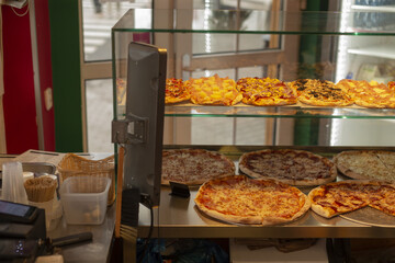 pizza counter with register and trays, cash area beside glass display filled with pies, staff workflow visible behind counter,