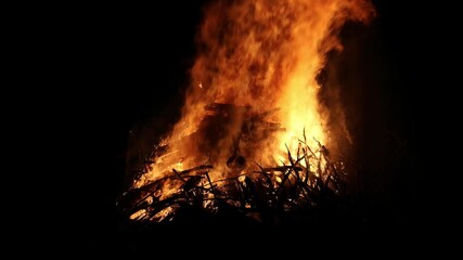 bonfire flames rising into dark night sky (bon fire flame orange yellow red glow glowing ember) sticks wood stick brush wooden fuel summer ceremony celebration enormous huge rise heat campfire camping