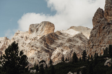 Typische Felsformationen der Dolomiten mit teils schneebedecktem Berg unter blauem Himmel und leichten Schleierwolken. Eindrucksvolle alpine Landschaft und klare Bergluft.