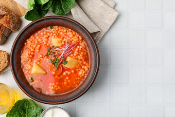 Tasty lentil soup in bowl served on white tiled table, flat lay. Space for text