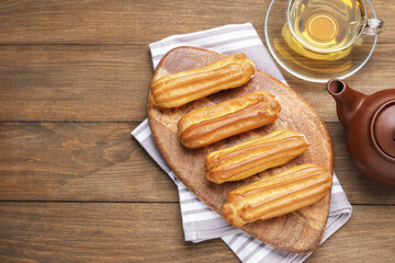 Tasty eclairs and tea on wooden table, flat lay. Space for text