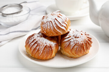Tasty profiteroles with powdered sugar served on white wooden table, closeup