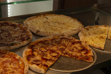 cheesy pizza slices on metal tray under glass, melted cheese and bubbling sauce on golden crust, close view of pepperoni