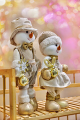 Snowman figurines dressed in festive attire, holding golden bells, surrounded by colorful bokeh lights, creating a joyful and enchanting holiday atmosphere with copy space