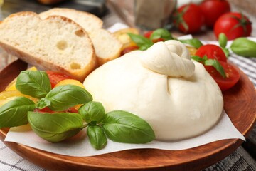 Delicious burrata cheese with basil, bread and tomatoes on wooden table, closeup