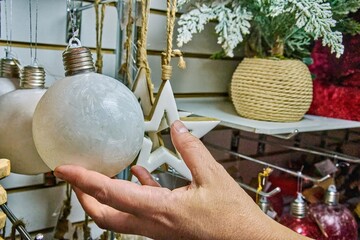 Light bulb-shaped toy ornament held by a hand in a festive Christmas toy store, surrounded by colorful decorations and holiday-themed items, creating a joyful atmosphere