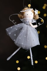 Naklejka premium Christmas decor. Fairy doll hanging on black background with blurred lights, closeup