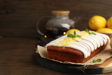 Tasty lemon cake decorated with icing, zest and mint served on wooden table, closeup. Space for text
