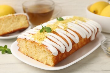 Tasty lemon cake decorated with icing, zest and mint served on white table, closeup