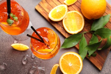 Glasses of refreshing spritzer cocktail, ice cubes and oranges on grey table, flat lay