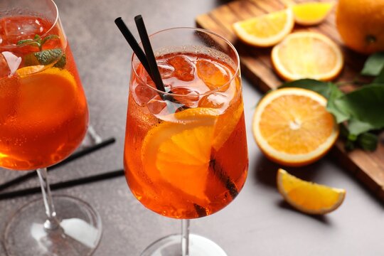 Glasses of refreshing spritzer cocktail and oranges on grey table, closeup
