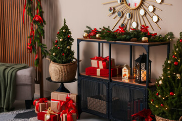 Shelving unit with Christmas decor between small spruce trees near beige wall indoors. Interior design
