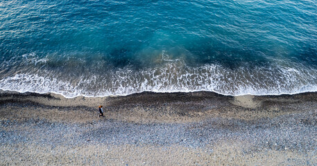 Person walking along beach coastline feeling solitude. Breaking waves on the beach
