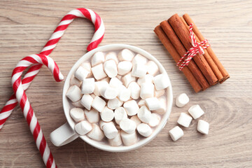 Tasty cocoa with marshmallows, candy canes and cinnamon on wooden table, flat lay. Christmas atmosphere