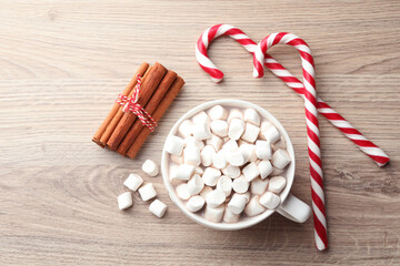 Tasty cocoa with marshmallows, candy canes and cinnamon on wooden table, flat lay. Christmas atmosphere. Space for text