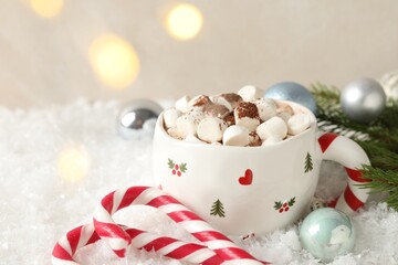 Tasty cocoa with marshmallows, candy canes and Christmas decor on artificial snow, closeup. Space for text