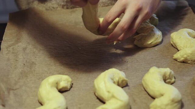 Hands of female baker working and placing dough of s-shaped yellow pastries, traditional Scandinavian holiday bakery desaturated footage easily color matched