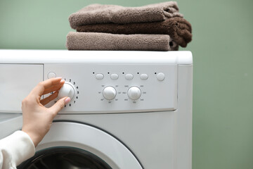 Woman turning on washing machine near green wall indoors, closeup