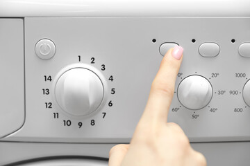 Woman pressing button on washing machine, closeup